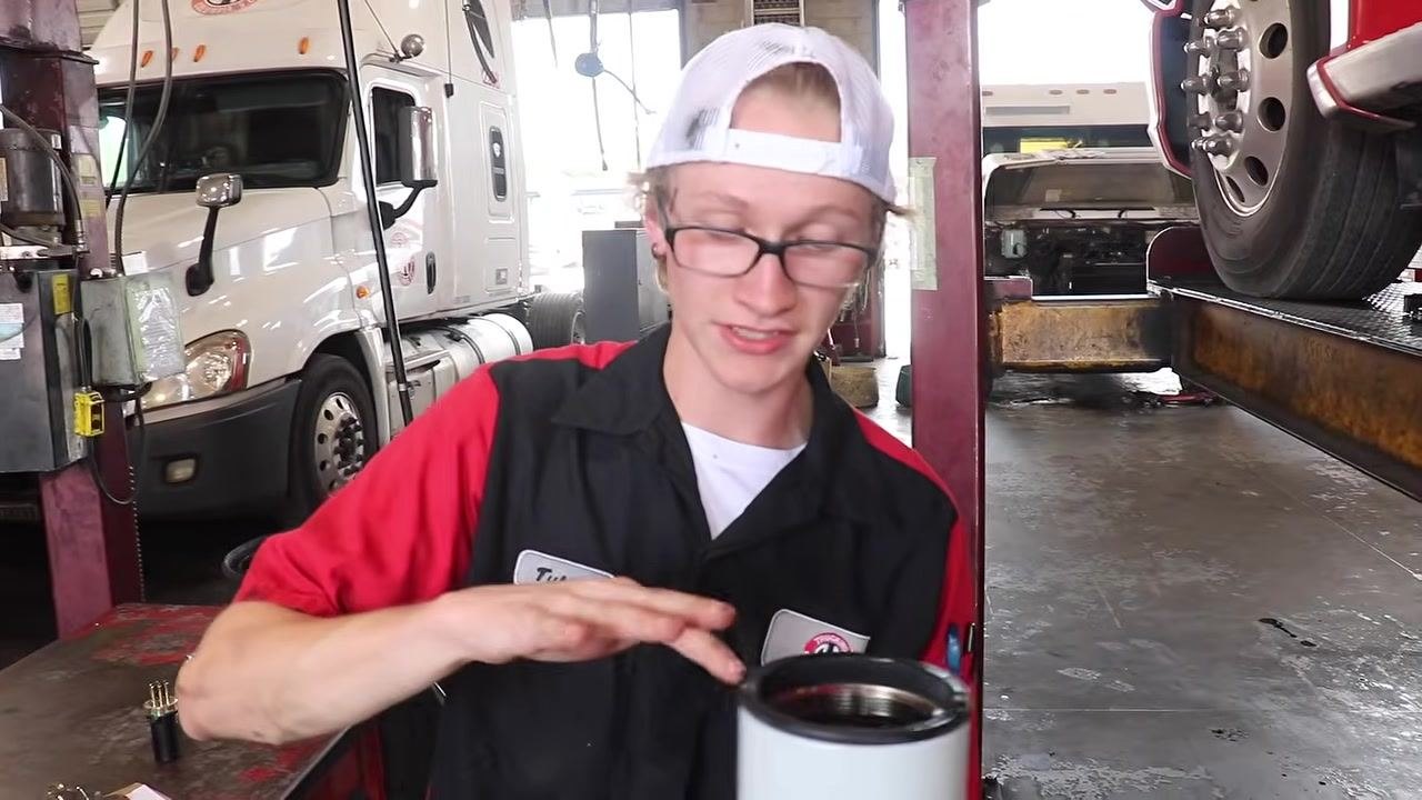 Technician under the truck using a filter wrench to tighten the newly installed oil filter.