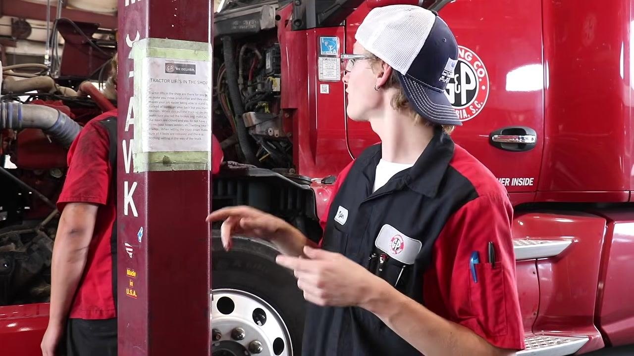 Technician holding a dipstick with a rag, showing the oil level to another technician near the open engine compartment.
