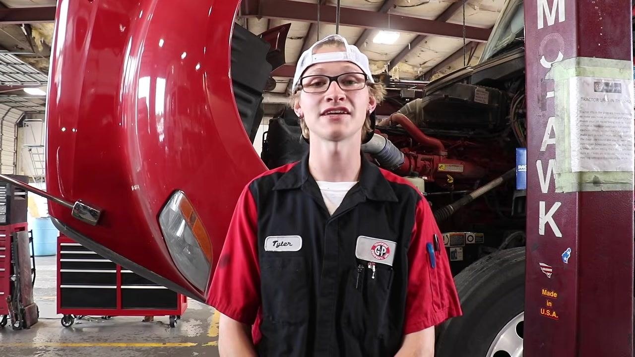 Technician in front of the truck, confirming that all fluids are at the correct levels. The truck and maintenance area are visible.