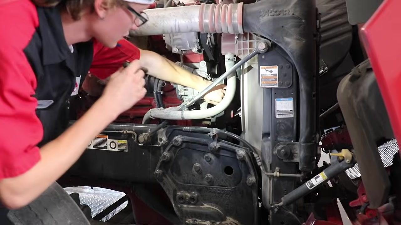 Mechanic reaching into the engine bay, pressing on the engine belts to check for cracks and proper tension.