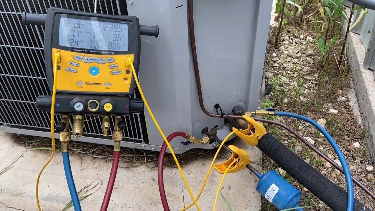 Close-up view of the Fieldpiece gauge display showing the superheat and subcooling values, with hoses and clamps still attached to the AC unit.