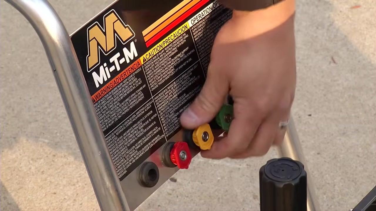 A person bending over the pressure washer, adjusting the choke lever on the engine while the spray gun and hoses remain connected.