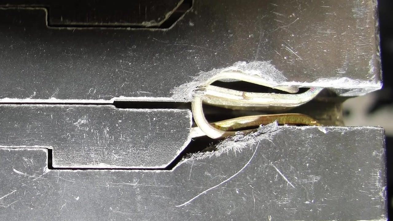 Close-up of a residential electrical panel with a hand gently tapping a breaker handle to test for weak springs, with labels such as "KITCHEN," "MUSIC STUDIO," and "DOWN STAIRS BEHIND STOVE" visible