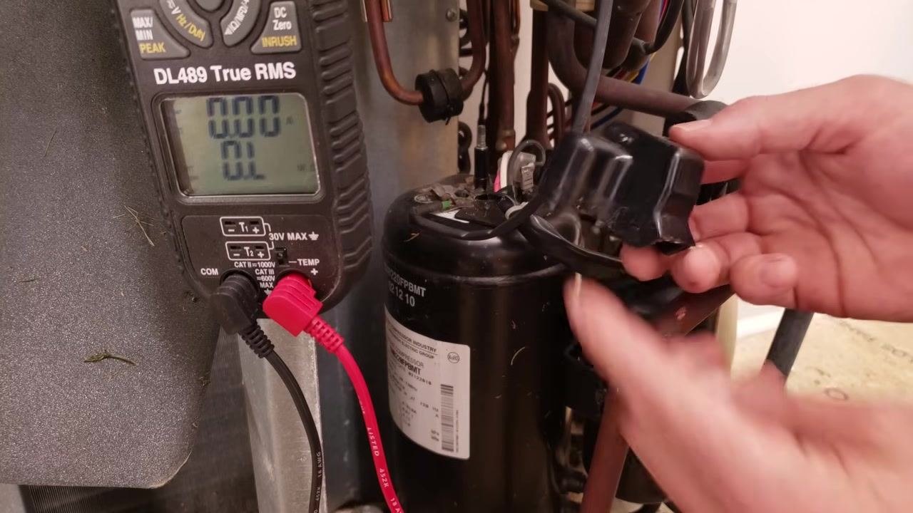 Technician removing the black plastic terminal cover from the mini-split compressor, with the multimeter still showing "OL"