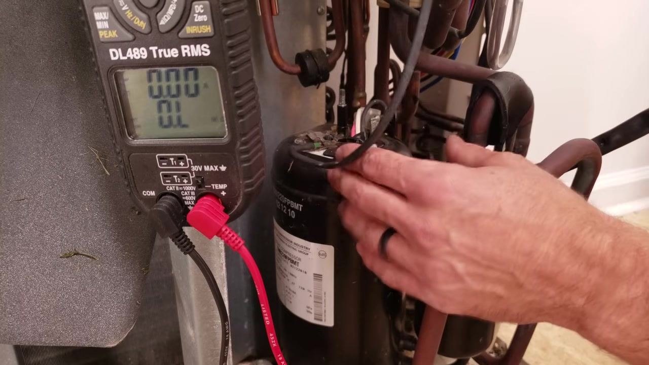 Technician's hands disconnecting wires from the compressor terminals, with the multimeter display showing "OL"