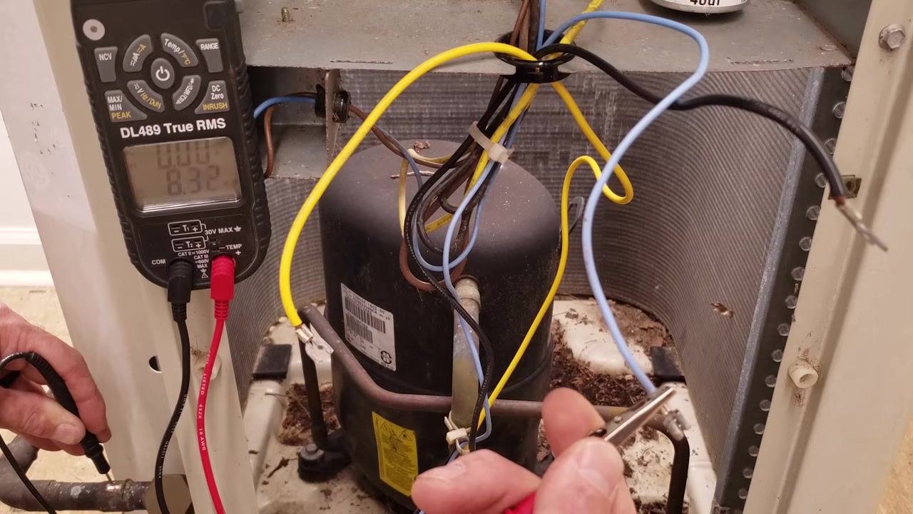 Multimeter showing a reading of 8.32 while the technician holds the probe against the compressor terminals