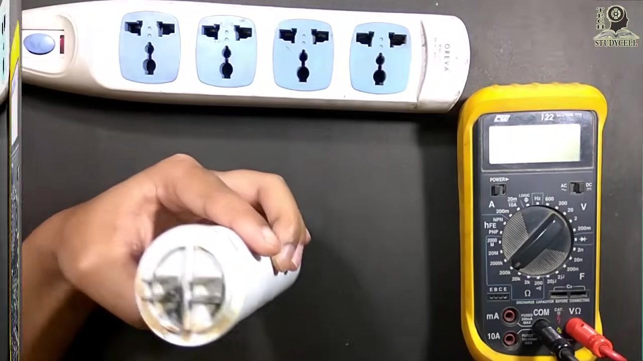 The capacitor terminals being shorted with a screwdriver to discharge it, with the multimeter and power strip visible