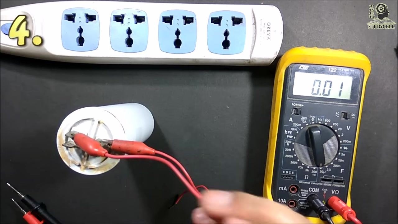 Alligator clips attached to the capacitor terminals, with the multimeter displaying "0.01" and a hand adjusting the setup