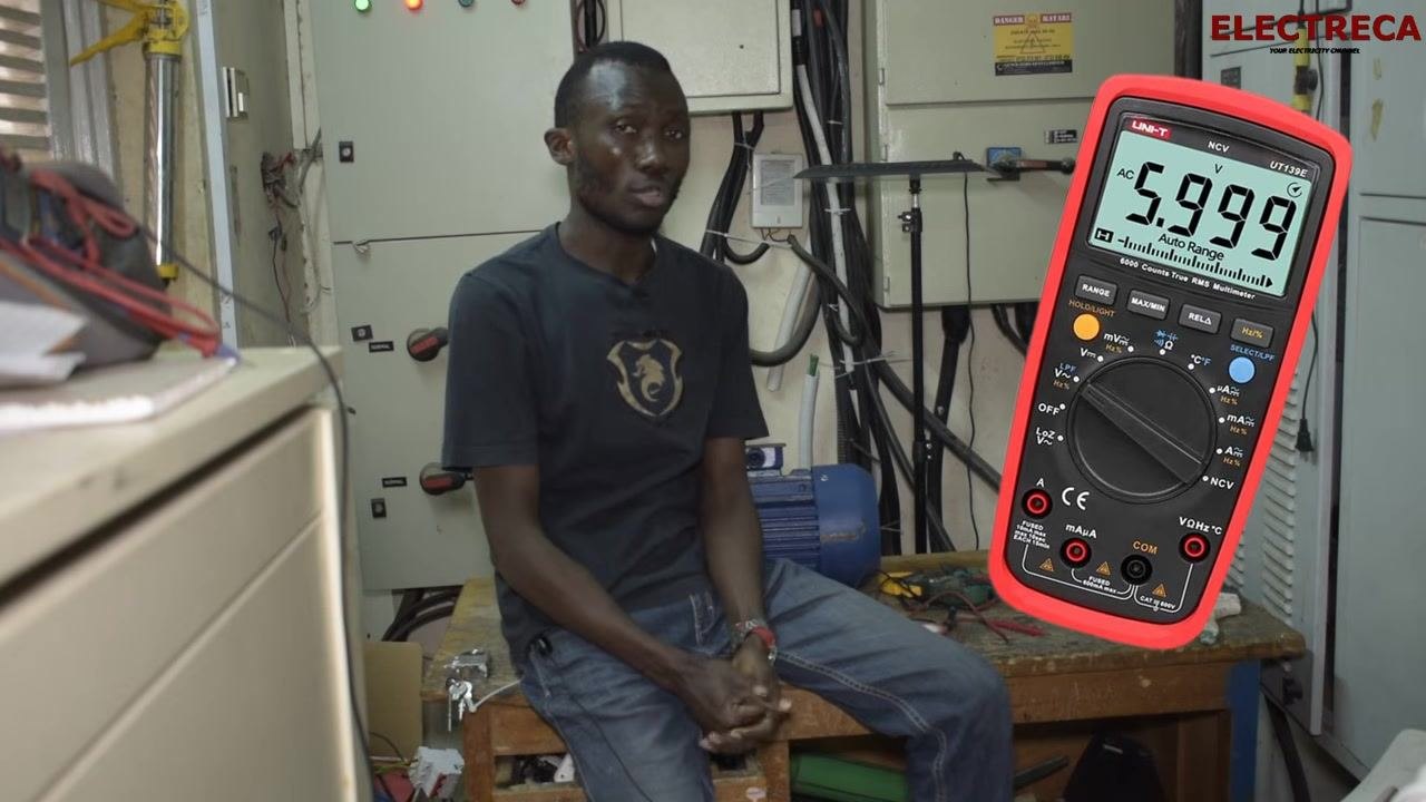 Workshop setup showing a motor and testing equipment on a workbench, with electrical panels and various tools in the background.