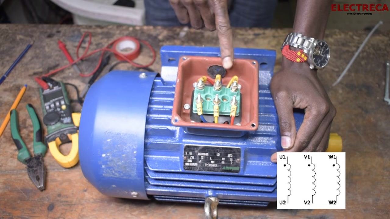 Close-up of the terminal box with labeled terminals and a winding diagram overlay for reference, with tools and a multimeter visible on the workbench.