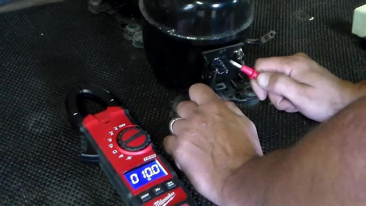 Measuring resistance across the bottom two terminals of a used compressor; multimeter displays 10.0 ohms
