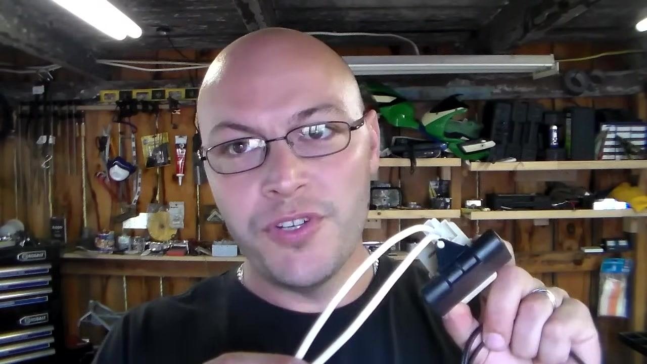 Holding a relay with two white wires to test voltage, workshop background with tools and shelves