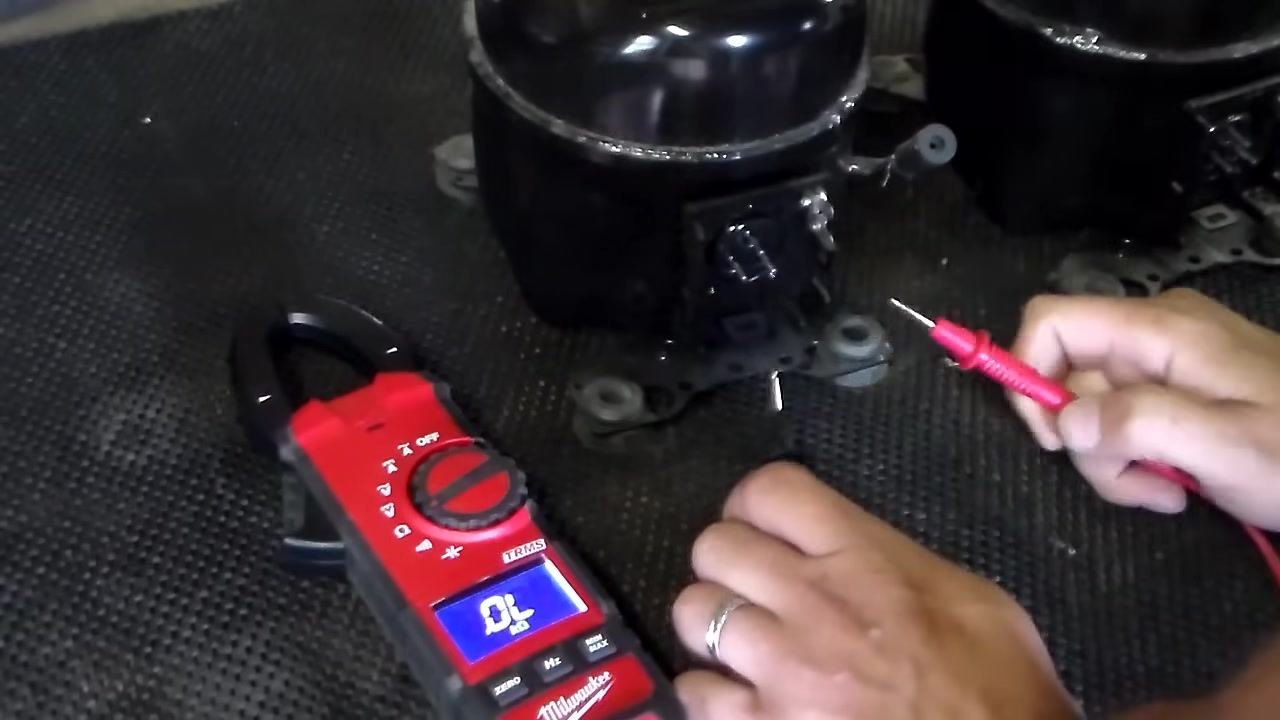 Digital multimeter set to ohms, displaying "OL," with test leads ready and compressor terminals visible
