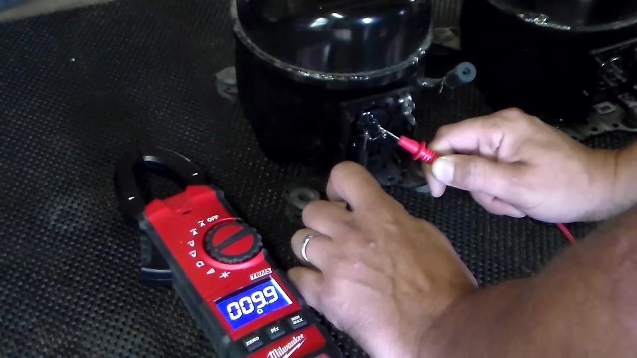 Measuring resistance across the bottom two compressor terminals; multimeter displays 9.99 ohms