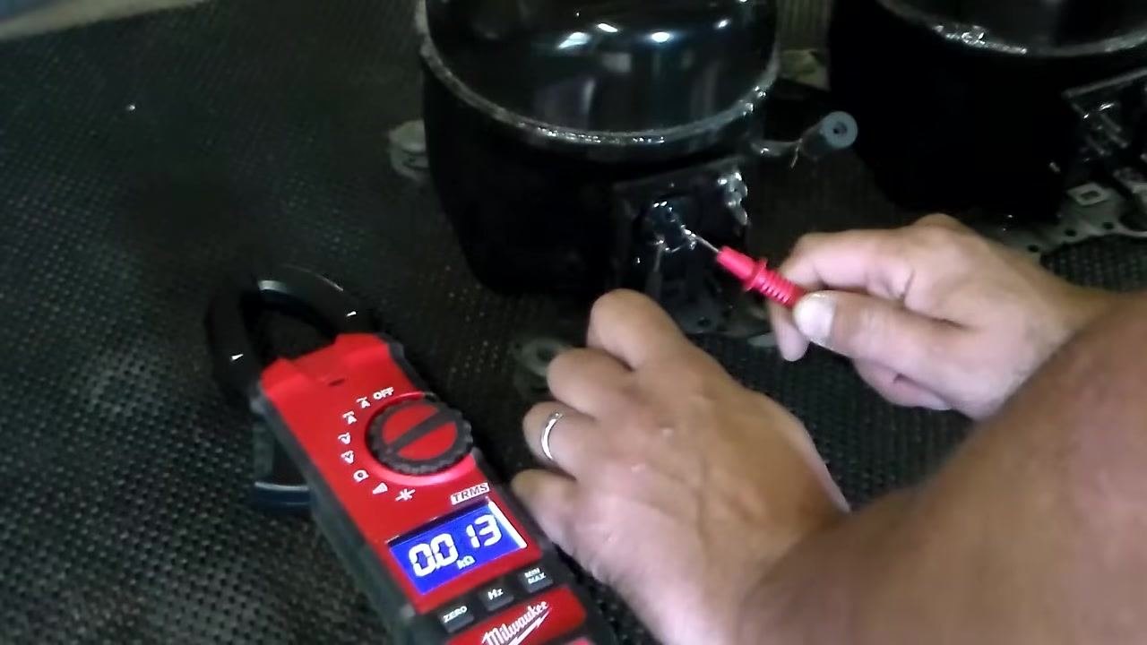 Repeating the resistance measurement on the bottom two compressor terminals; multimeter displays a low ohm reading consistent with the first test