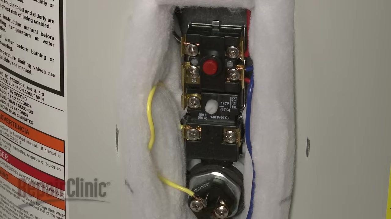 Upper thermostat exposed with the red reset button visible, surrounded by insulation, with warning and energy labels on the water heater
