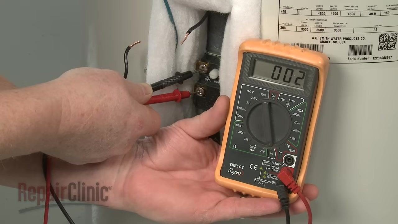 Technician holding a digital multimeter and placing probes on the lower thermostat terminals, insulation pulled aside, yellow and blue wires visible