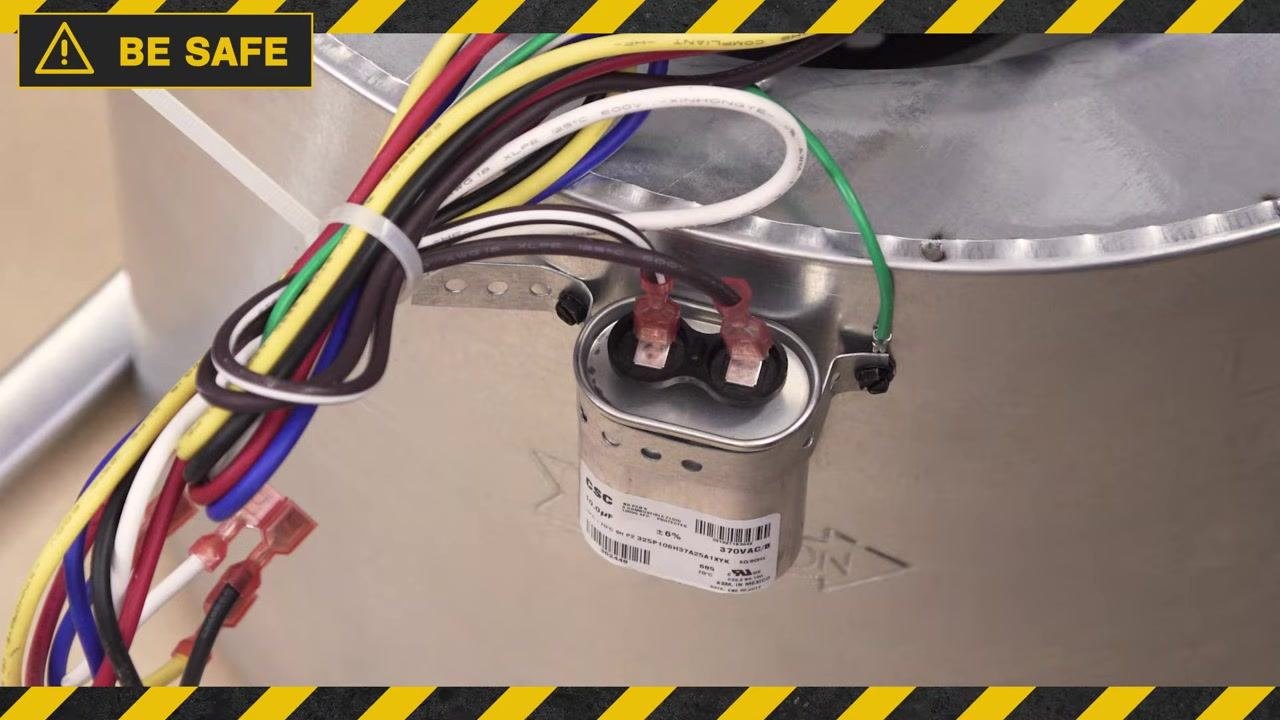 Run capacitor placed on a wooden work surface, ready to be discharged, with a safety warning banner