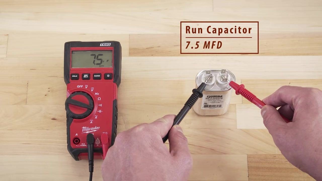 Hand using an insulated screwdriver to short terminals on a dual run capacitor, with a safety warning banner
