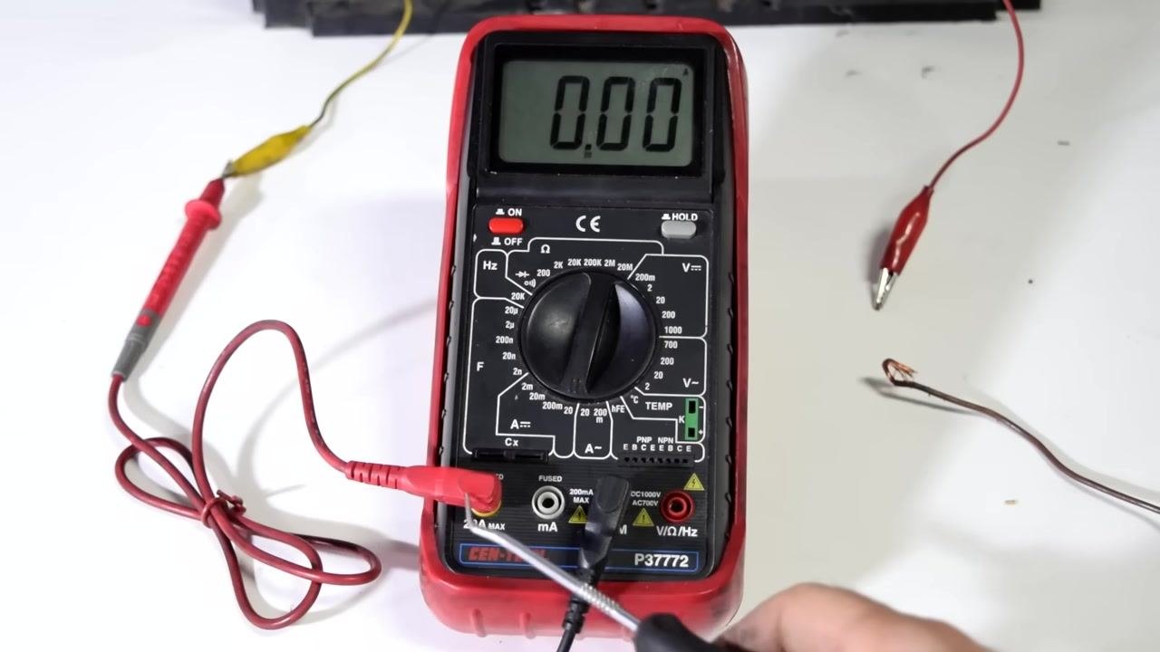 Close-up of multimeter ports, with the red lead in 20A MAX and the black lead in COM, and a screwdriver pointing at the ports.