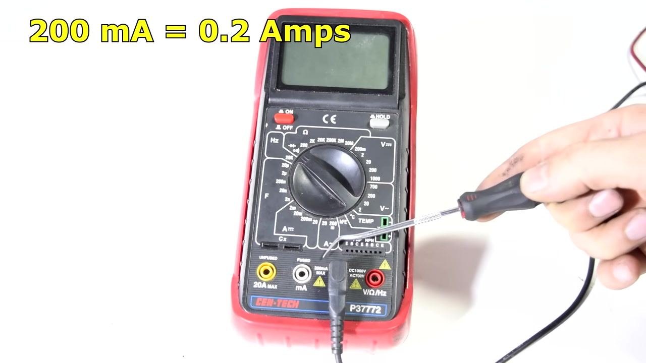 Hand using a screwdriver to point at current measurement settings on the multimeter dial.