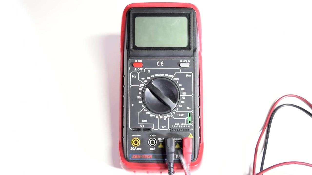 Multimeter connected to a wire harness, with a finger pointing to a section of the wire showing possible damage.