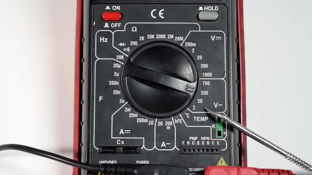 A digital multimeter with both test leads inserted, display reading 0.00, shown against a clean white background with a small tool visible nearby.