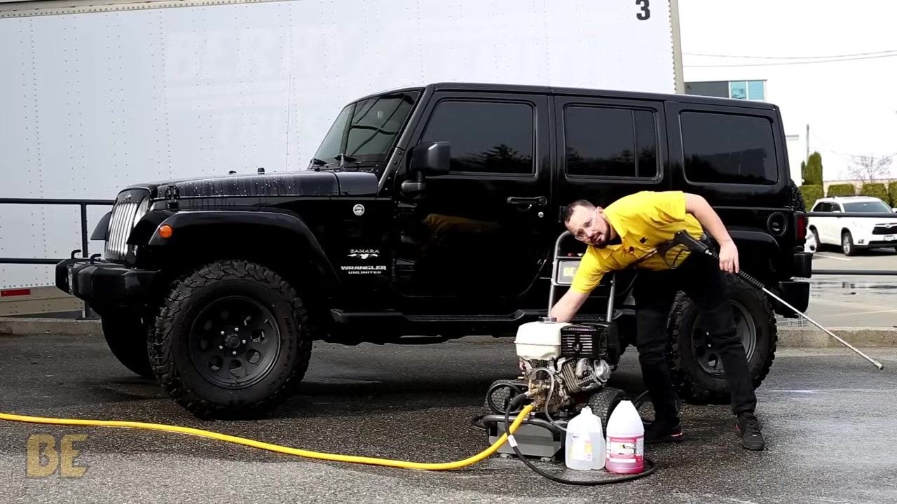 Person in a yellow shirt turning off the BE Power Washer, holding the spray wand next to the black Jeep Wrangler
