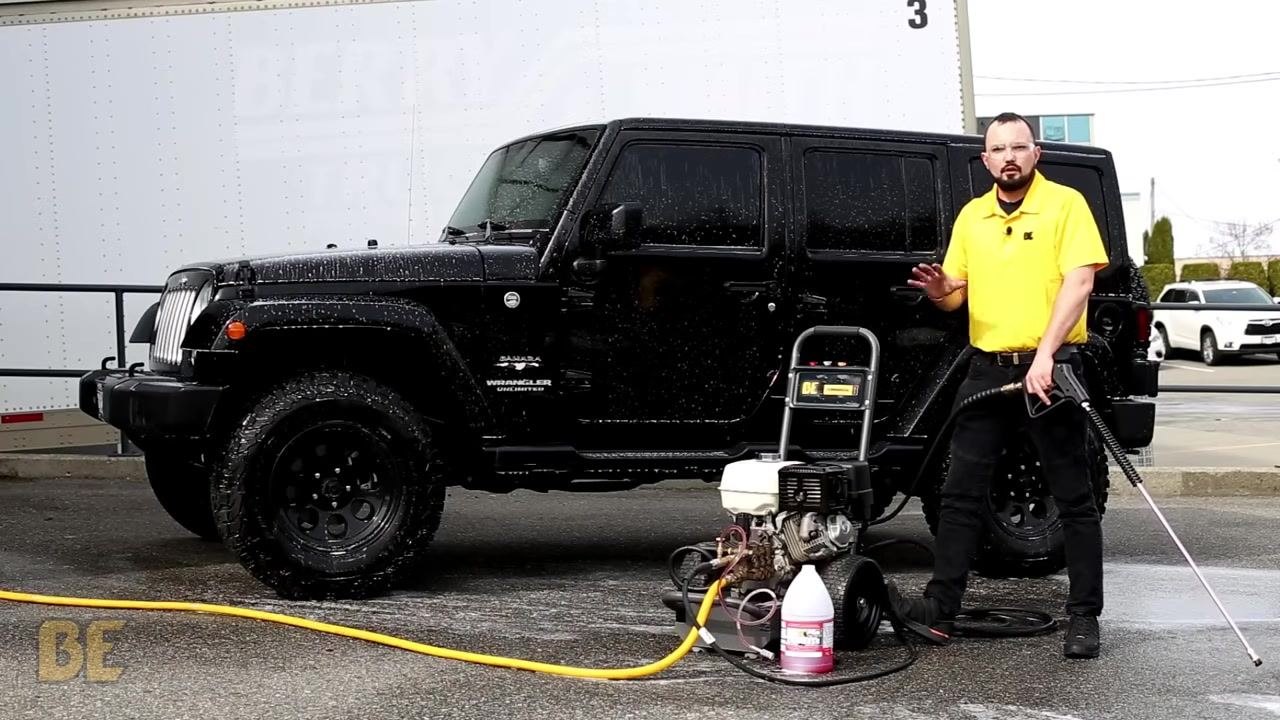 Person in yellow shirt rinsing the upper part of a black Jeep Wrangler with a BE Power Washer. Water spray is visible on the vehicle.