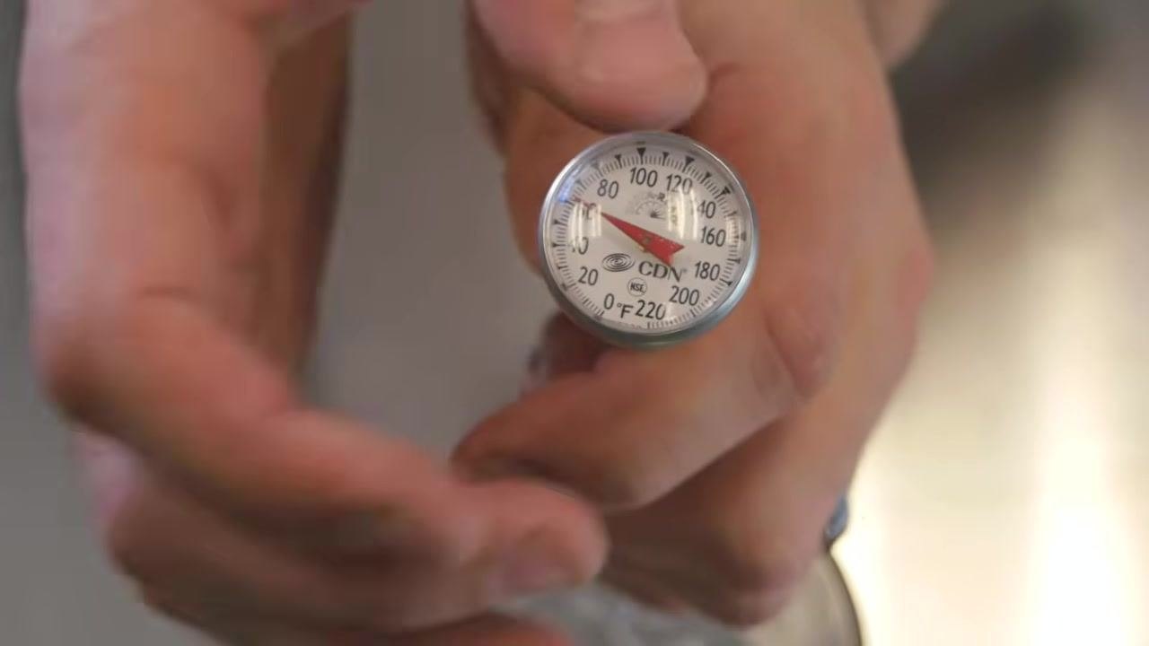 Hands using the sheath as a wrench to adjust the calibration nut on the thermometer, above a glass of ice water