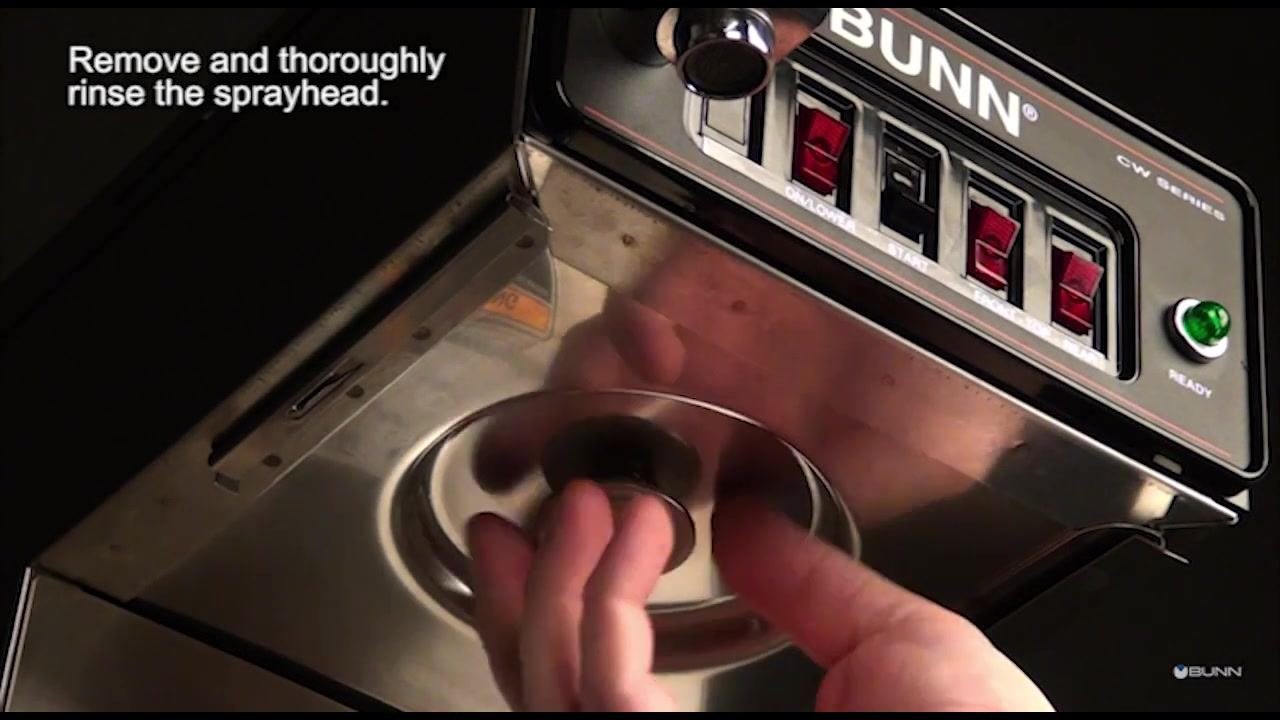 A hand removes the spray head from the underside of the coffee brewer.