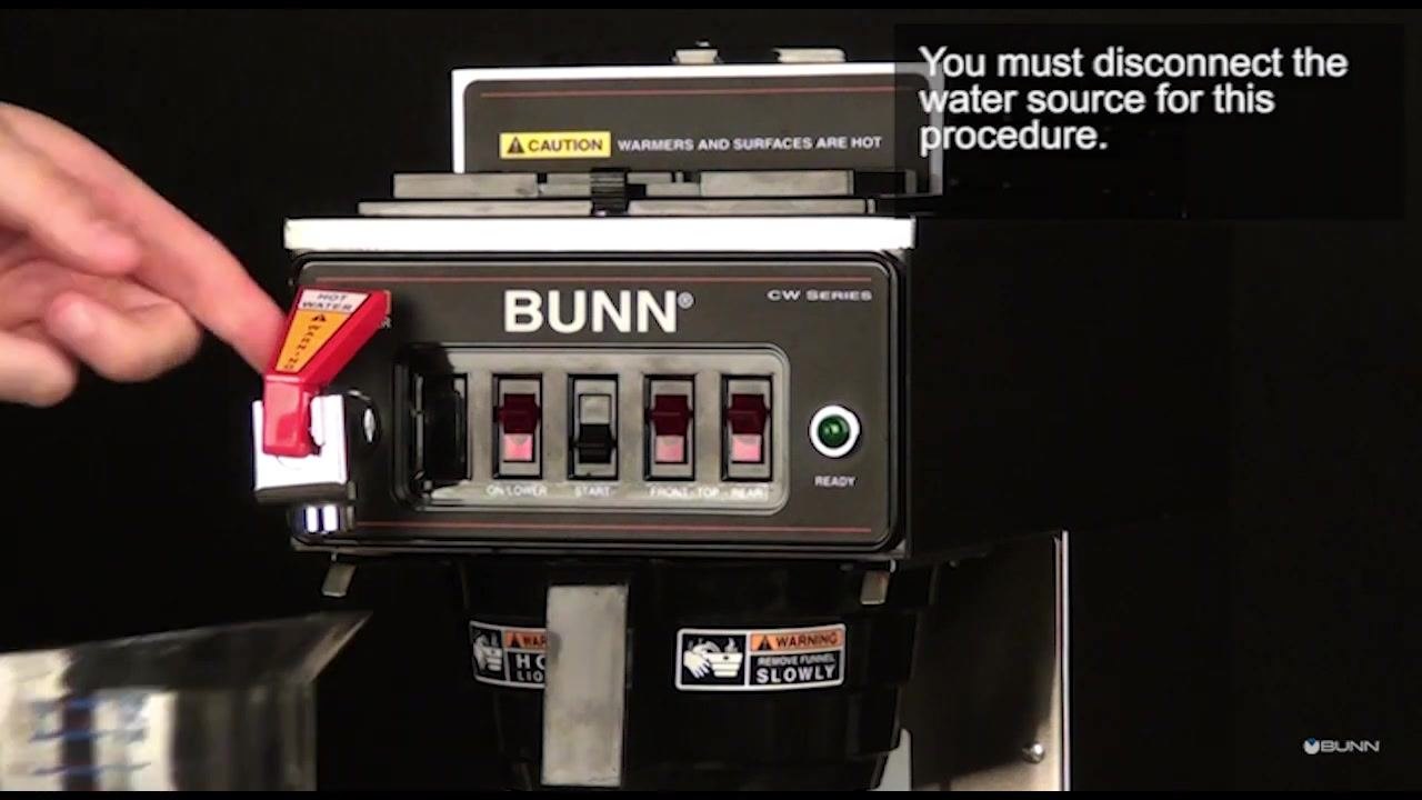 A hand operates the hot water faucet lever on the coffee brewer to drain remaining water.