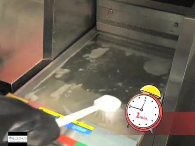 A gloved hand using a long-handled brush to scrub the fryer vat. A timer icon on screen shows "2 min."