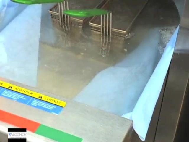 Fryer vat filled with cleaning solution and blue towels draped over the sides, fryer baskets submerged, and a green tool visible.