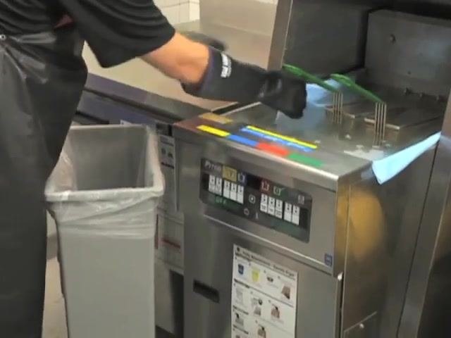 A person wearing gloves and an apron discards blue towels from the fryer into a trash can.