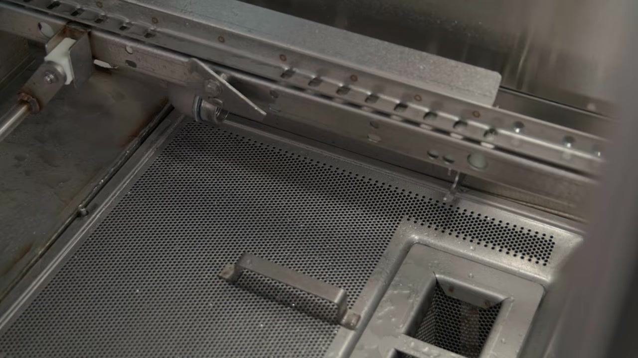 Close-up of the wash tank bottom showing water spray flushing debris toward the strainers