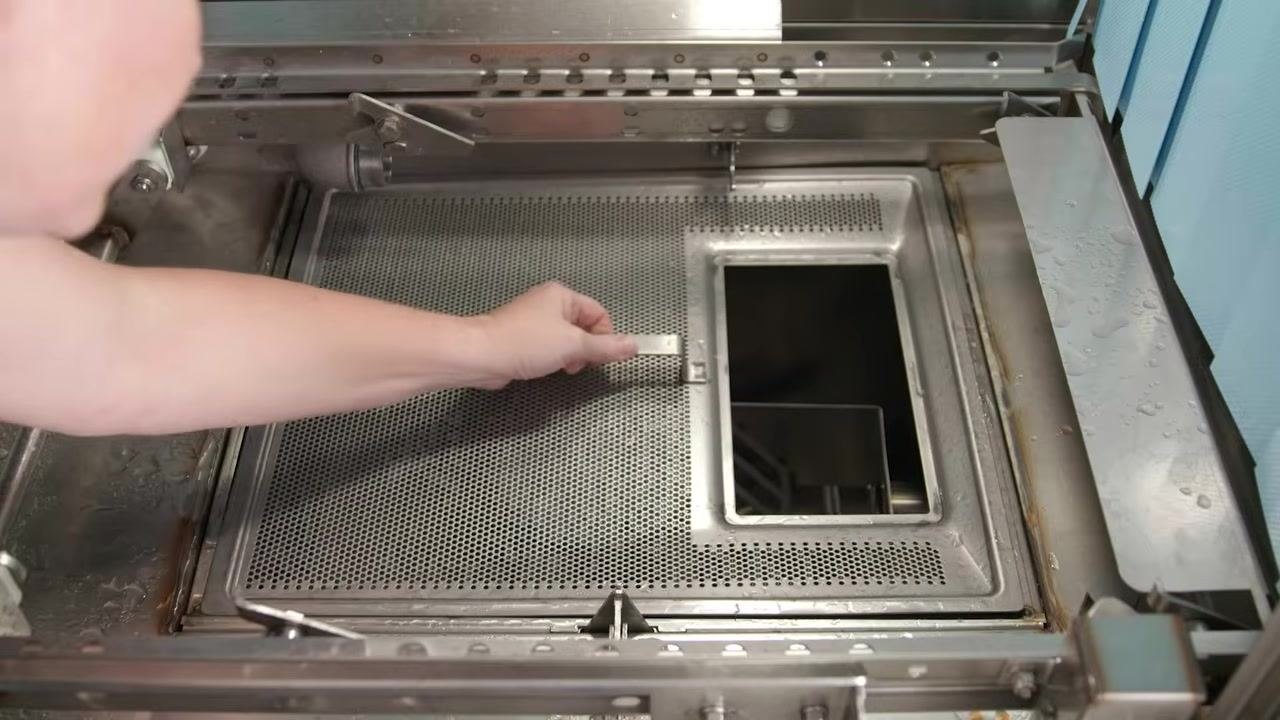 Person reinstalling the strainer pan and scrap basket inside the machine
