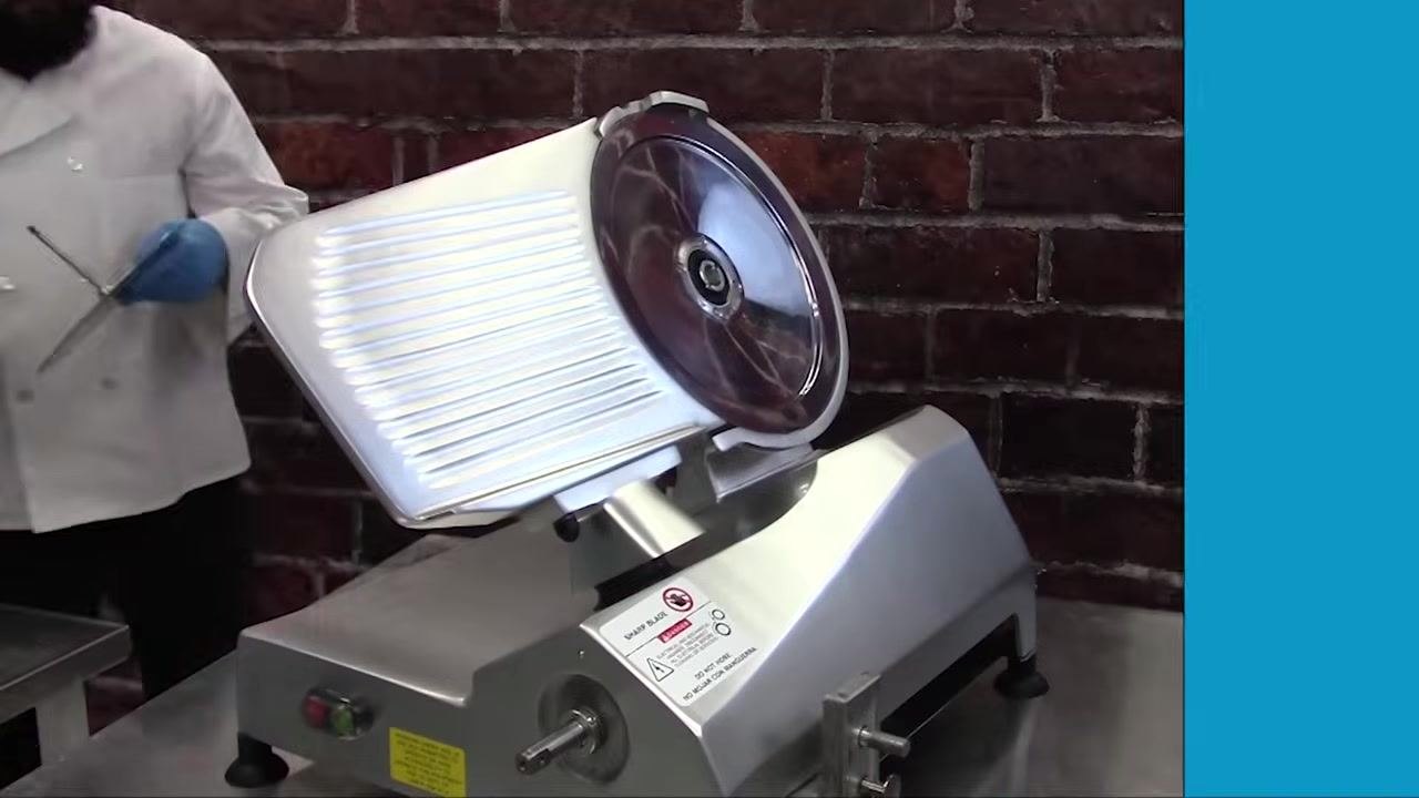 Close-up of the operator reinstalling the knife scraper on the slicer, showing the adjustment knobs and scraper mechanism.
