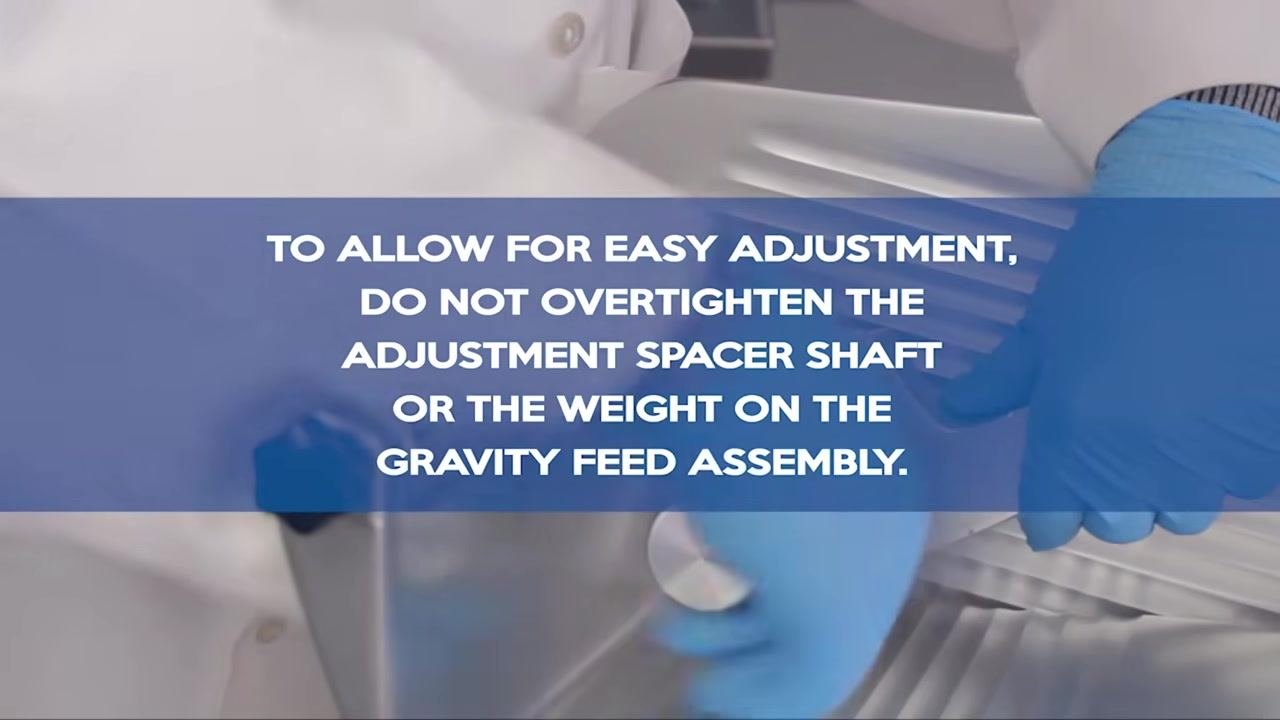 Instructional overlay reading "TO ALLOW FOR EASY ADJUSTMENT, DO NOT OVERTIGHTEN THE ADJUSTMENT SPACER SHAFT OR THE WEIGHT ON THE GRAVITY FEED ASSEMBLY," with blue gloves and slicer components visible in the background.