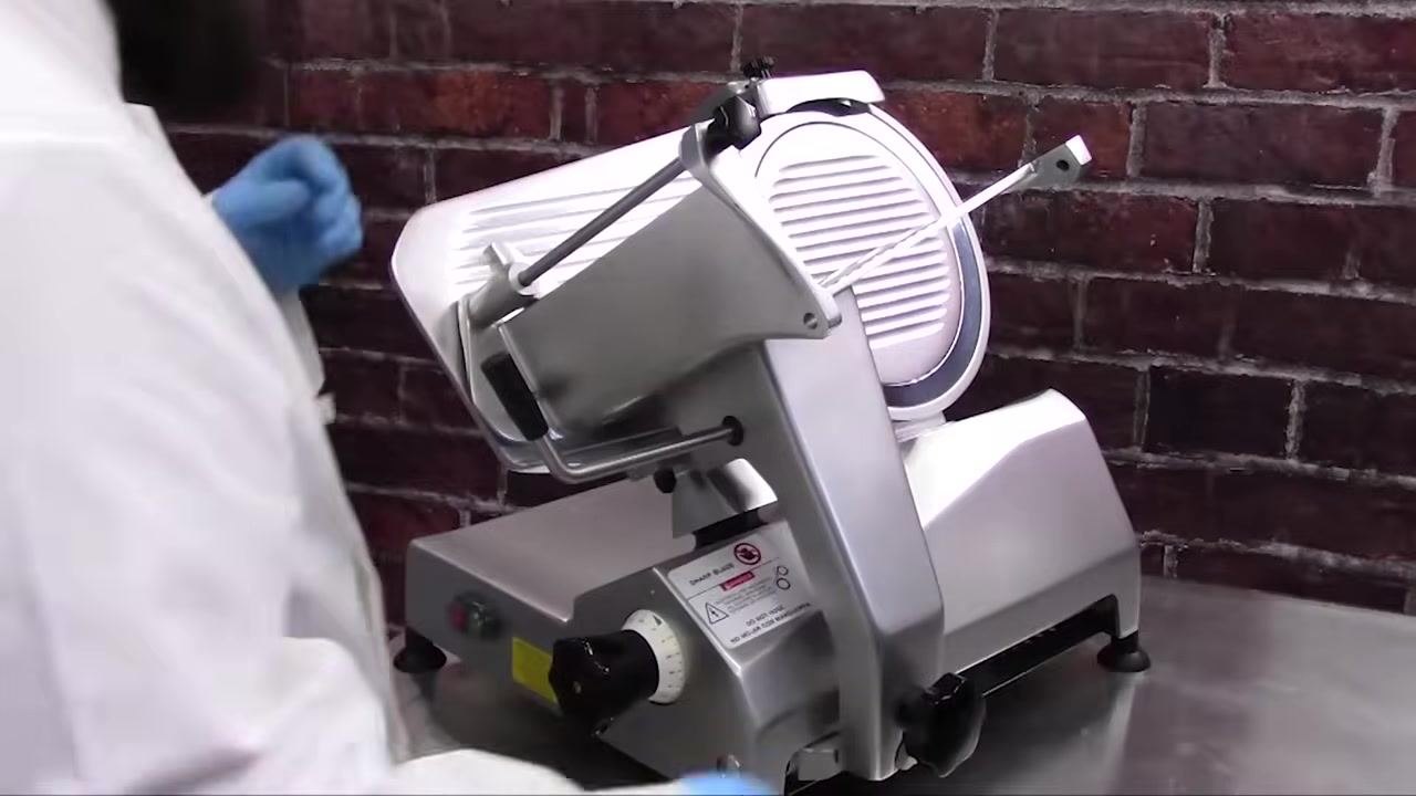 Operator turning the feed weight counterclockwise to remove it from the slicer, with the feed grip and support arm visible.