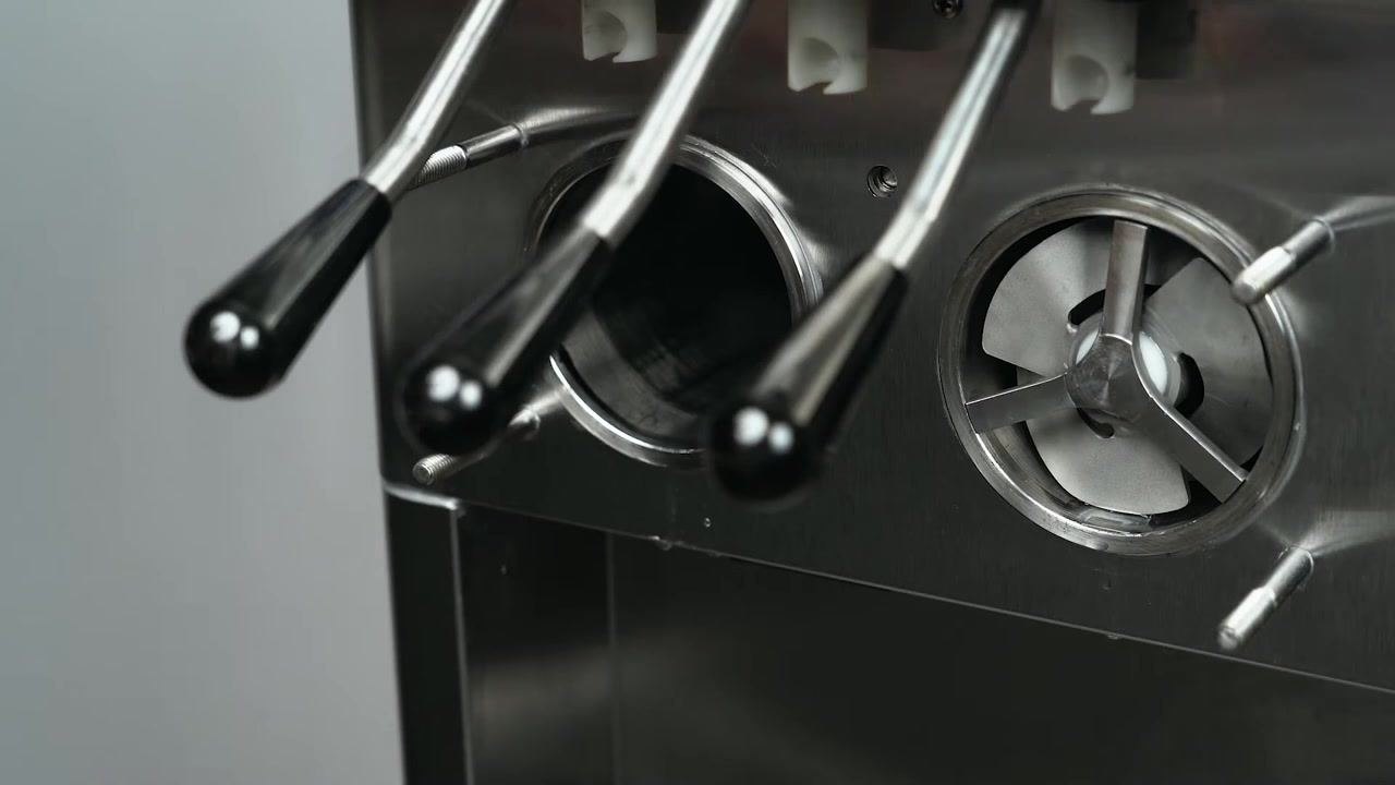 Hands pulling the auger assembly out of the freezing cylinder of the machine, with visible black handles and stainless steel front panel