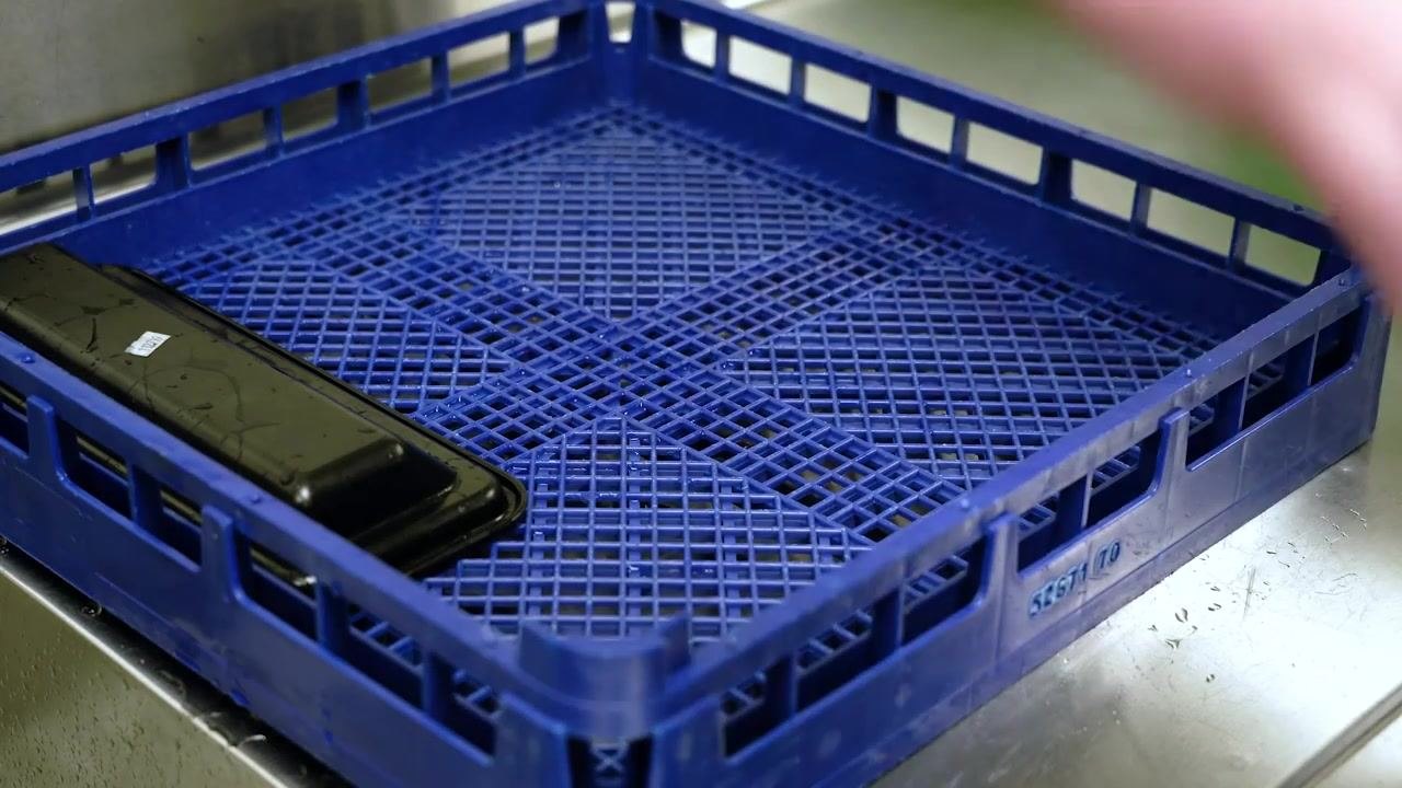 A blue plastic drying rack/tray on a stainless steel surface, with a single black machine part placed on it, showing water droplets and a clean environment suitable for air drying sanitized equipment