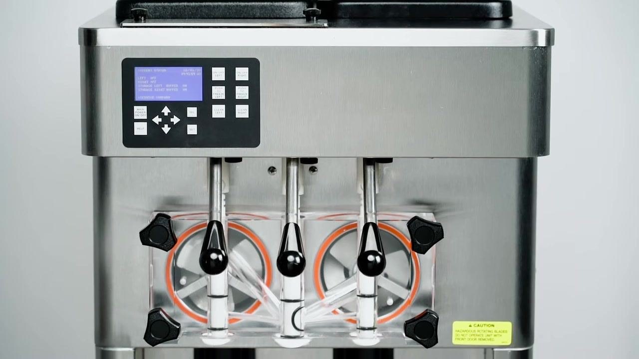 A person's hands removing the black drip tray from the lower section of a stainless steel soft serve machine. The environment is a clean, industrial kitchen setting.