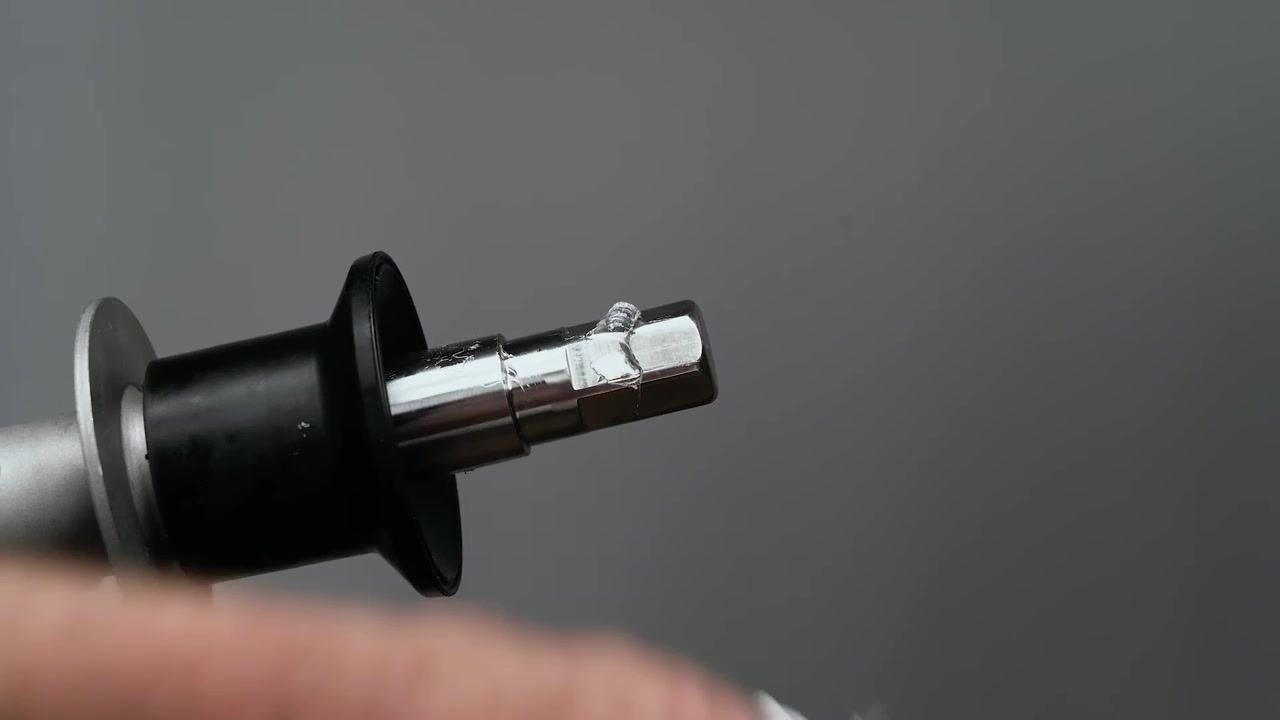 A close-up of a stainless steel auger shaft with a black rear seal installed. The seal and the shaft are coated with a visible layer of clear lubricant. The background is neutral gray, and a hand is partially visible holding the shaft.
