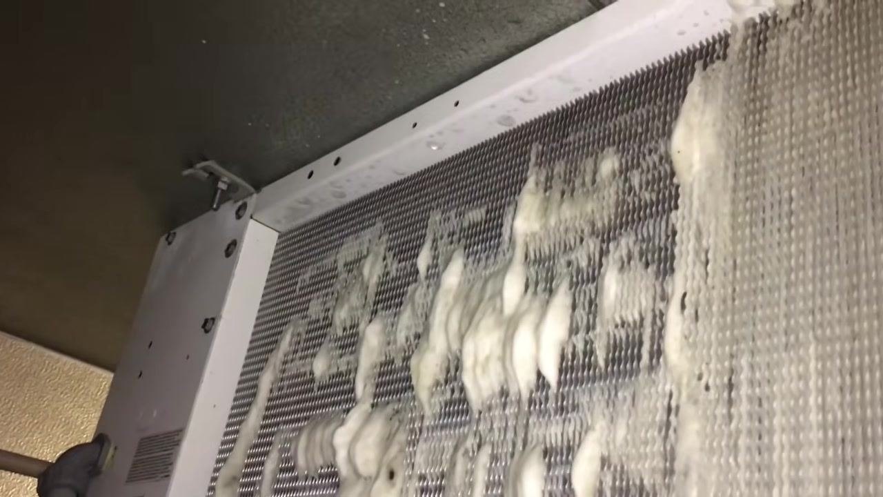 Close-up of the evaporator coil with foaming cleaner applied, showing dirt and buildup on the fins