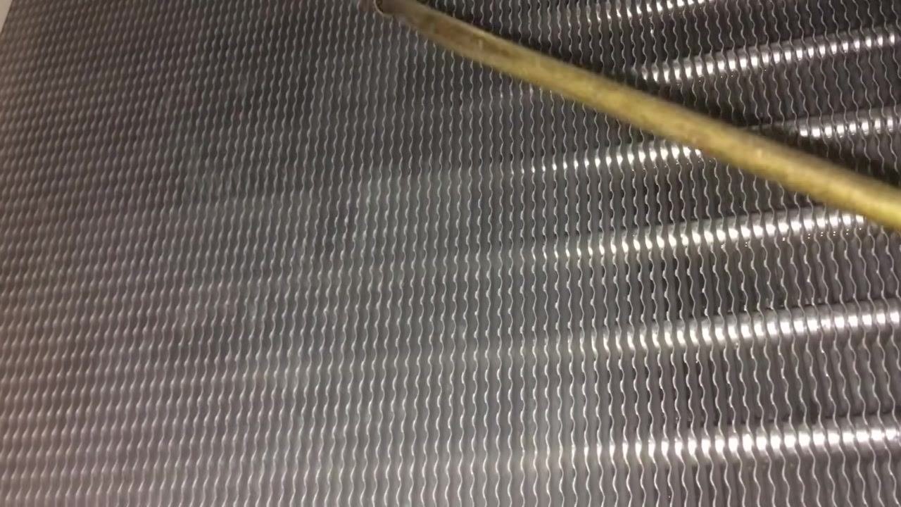 Close-up of clean evaporator coil fins with a brass rod pointing at the metallic, wavy surface