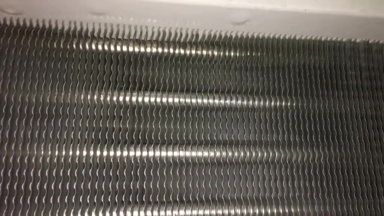 Close-up of evaporator coil fins showing a clean surface with minor spots and a uniform wavy pattern