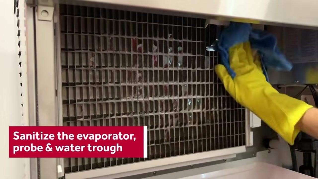 Person wearing yellow gloves wiping down the evaporator cover in a sink with a blue cloth, with the on-screen instruction "Sanitize the evaporator cover"