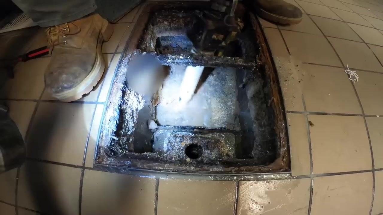 Close-up of the inside of a grease trap, showing a white pipe along with residual liquid and debris.