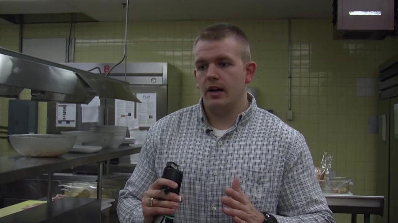 A person holding a thermometer in a commercial kitchen, preparing to measure hot food temperature